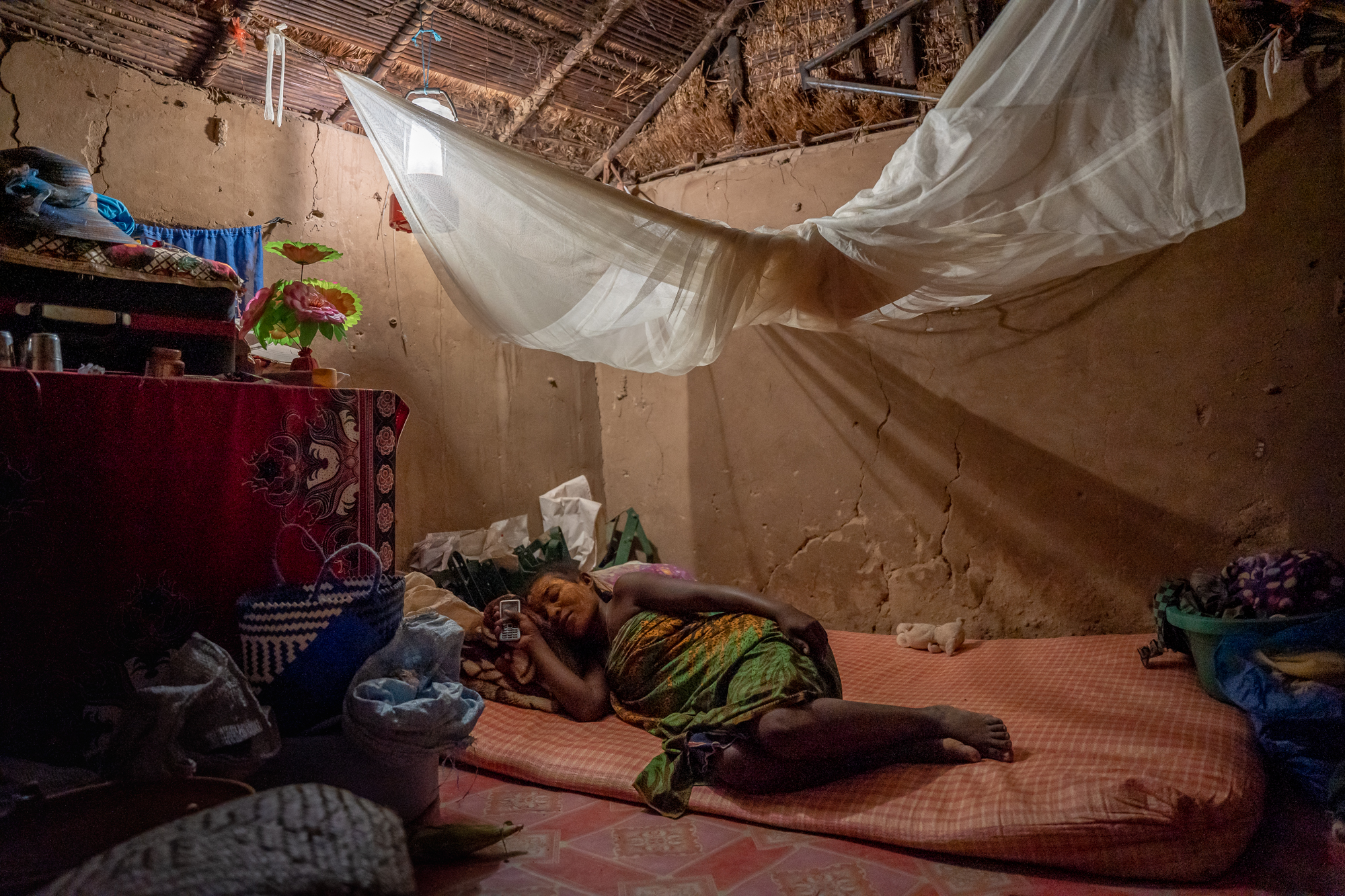 A woman rests inside her illuminated hut.